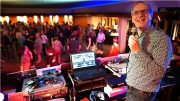 Ein DJ steht an seinem Mischpult vor der Menge tanzender Menschen.