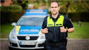 Ein Polizist steht vor seinem Dienstwagen