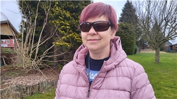 Eine Frau steht im Freien und trägt eine Sonnenbrille - als Schutz vor dem Sonnenlicht, das für sie als fast Blinde zu grell ist.