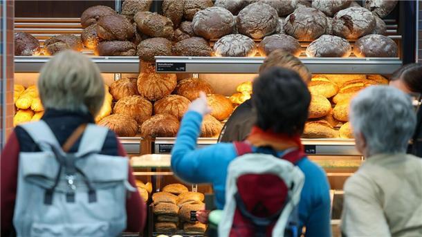 Kunden stehen in der Bäckerei und kaufen Brote. 