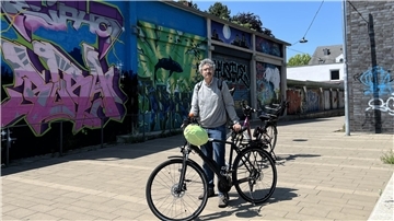Ein Mann steht mit seinem Fahrrad vor einer Graffitiwand.