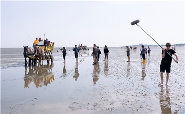 Dreharbeiten im Watt vor Cuxhaven mit nackten Füßen: Regisseur André Erkau (Zweiter von links auf Wattwagen) und das Filmteam besprechen die nächste Einstellung für die Komödie, die den Arbeitstitel „Der Lux“ trägt.