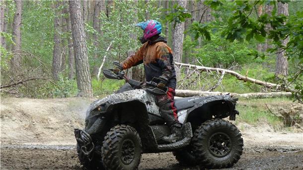 Eine Frau steht in dreckiger Kleidung auf einem dreckigen Quad.