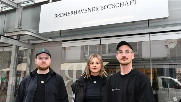 Drei Leute vor einem gläsernen Pavillon. 