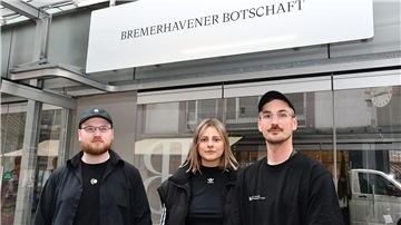Drei Leute vor einem gläsernen Pavillon. 