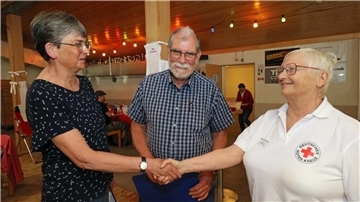 Zwei Frauen geben sich die Hand. Ein Mann steht etwas versetzt zwischen ihnen. 