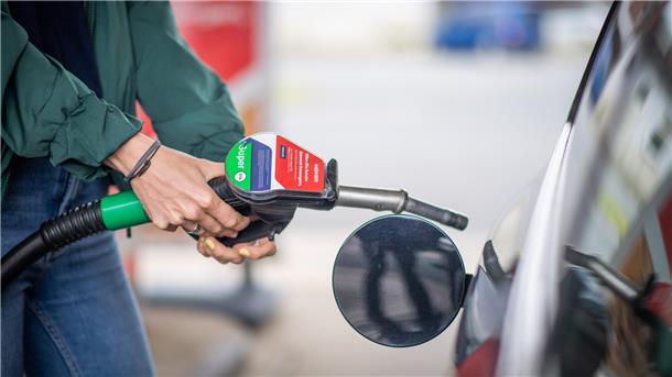 Körper einer Person im Anschnitt. Die Person ist gerade dabei, ein Auto zu tanken. 