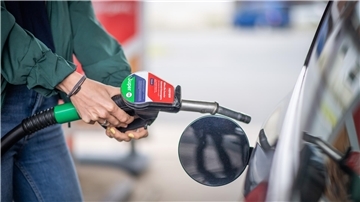 Körper einer Person im Anschnitt. Die Person ist gerade dabei, ein Auto zu tanken. 
