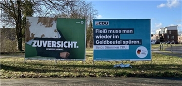 Zwei große Plakate stehen auf einer Wiese.