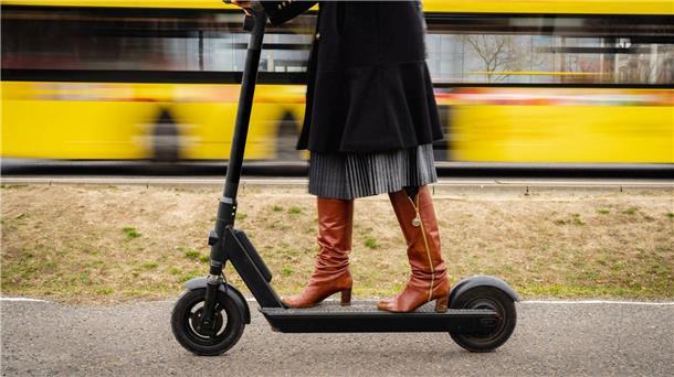 Frau fährt mit einem E-Tretroller, im Hintergrund ist ein vorbeifahrender Bus zu sehen.
