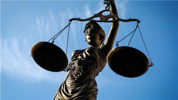 Justizia hält eine Waage vor blauem Himmel in der Hand.