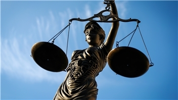 Justizia hält eine Waage vor blauem Himmel in der Hand.