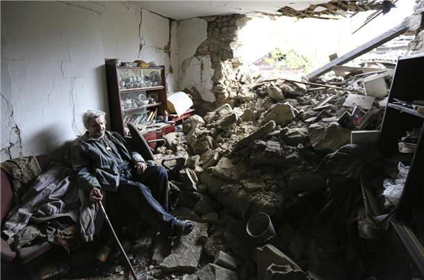 Ein älterer Mann sitzt auf einem Sofa in einem durch Beschuss beschädigten Haus im ukrainischen Kriegsgebiet.