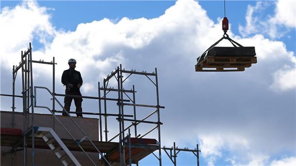 Ein Arbeiter dirigiert auf einer Baustelle einen Kran.