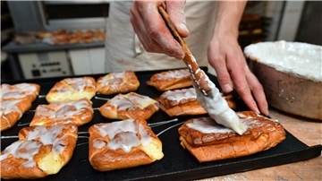 Ein Bäckermeister pinselt Zuckerguss auf süßes Gebäck in seiner Backstube.