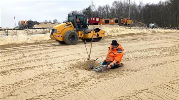 Ein Bauarbeiter untersucht, ob der Sand auf der aufgefüllten Baugrube bereits ausreichend verdichtet. 