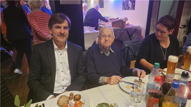 Rudi Prehn (Mitte) ist von zwei Menschen umgeben und sitzt an einem Tisch.