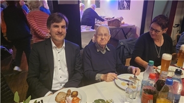 Rudi Prehn (Mitte) ist von zwei Menschen umgeben und sitzt an einem Tisch.