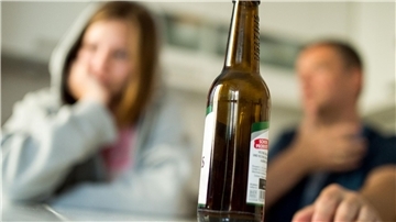 Bierflasche im Vordergrund, im Hintergrund zwei Menschen. 