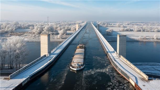 Ein Binnenschiff überquert in einer Fahrrinne das vereiste Wasserstraßenkreuz Magdeburg. Der Mittellandkanal führt an dieser Stelle in einer Trogbrücke über die Elbe.