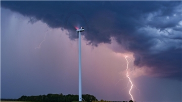 Ein Blitz leuchtet am Abendhimmel hinter einer Windenergieanlage im Osten Brandenburgs.