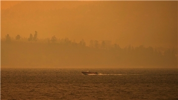 Ein Boot fährt auf dem Okanagan-See, während der Rauch des McDougall-Creek-Wildfeuers über dem Gebiet liegt.
