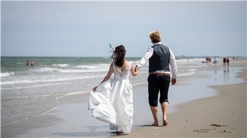 Ein Brautpaar geht nach der Trauung am Strand von Juist entlang.