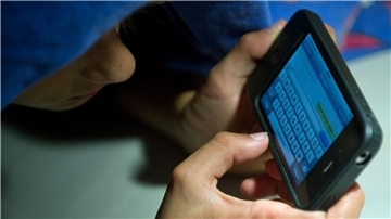 Ein elfjähriger Junge liegt unter der Bettdecke und schreibt auf einem Smartphone eine SMS. Kinder unter 13 Jahren sollten Experten zufolge keinen Zugang zu derartigen Medien haben.