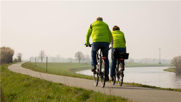 Ein Fahrradfahrer und eine Fahrradfahrerin sind auf dem Weser-Radweg unterwegs. Wer eine solche Tour plant, kann sich in einem neuen Wanderführer für das 2025 informieren.