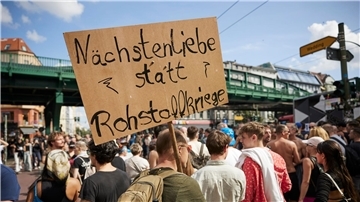 Ein Feiernder trägt ein Schild mit der Aufschrift „Nächstenliebe statt Rohstoffkriege“ bei der Technoparade Zug der Liebe durch Berlin.