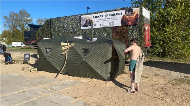 Ein Festival-Besucher steht vor einer mobilen Front-Sauna, die in Estland für die ukrainische Armee entwickelt worden ist.
