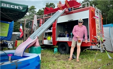 Ein Feuerwehrauto mit Matratzen, einem Sofa auf dem Dach und einer Rutsche sorgt auf dem Campingplatz für Partystimmung.