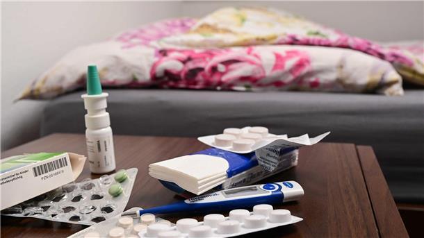 Krankheitswelle rollt: Arztpraxen und Kliniken am Limit Ein Fieberthermometer und Medikamente liegen auf einem Nachttisch.
