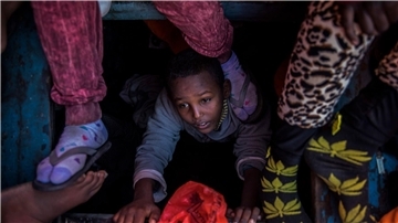 Ein Flüchtlingskind aus Eritrea versucht an der Küste zu Libyen, an Bord eines überfüllten Holzbootes hinaufzuklettern.