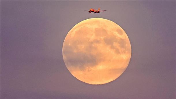 Ein Flugzeug fliegt vor dem sogenannten Supermond am frühen Abend über Leipzig.