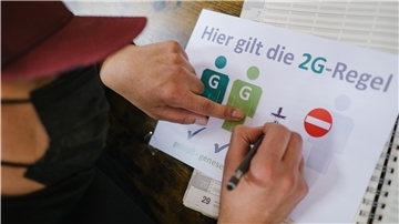 Ein Friseur zeichnet ein "+" auf ein Schild, das auf die 2G-plus-Regel hinweisen soll.