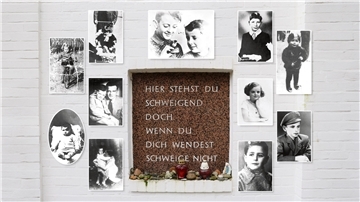 Bilder von Kindern sind auf einer Mauer rund um eine Inschrift platziert. Sie lautet: Hier stehst Du schweigend, doch wenn Du Dich wendest, schweige nicht