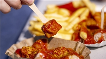 Ein Genussmoment im Zeichen der Tradition – eine Person genießt eine Currywurst zum 75. Jahrestag ihrer Erfindung. Ein kulinarisches Kulturerbe, das deutschlandweit begeistert.