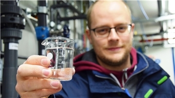 Ein Mann hält ein Glas mit Wasser in die Kamera. Es handelt sich um gereinigtes Abwasser, das für die industrielle Produktion bei Kronos Titan verwendet werden soll.