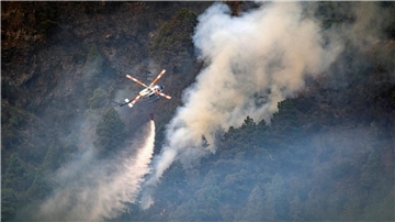 Ein Hubschrauber wirft Wasser auf die Flammen, während sich das Feuer durch den Wald in Richtung der Stadt Pinolere ausbreitet.