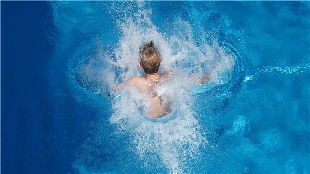 Ein Junge springt in einem Freibad ins Wasser.