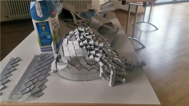 Ein kunstvoller Helm, der aus alten Milchtüten gebastelt wurde, liegt auf einem Tisch.