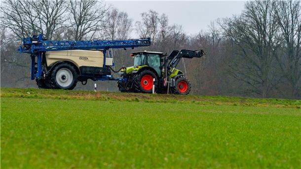 Ein Landwirt fährt mit seinem Trecker samt angehängter Spritze über eine Straße.