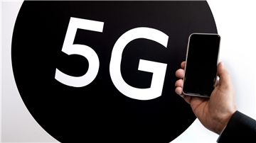 Ein Mann hält ein Smartphone neben ein 5G-Plakat.