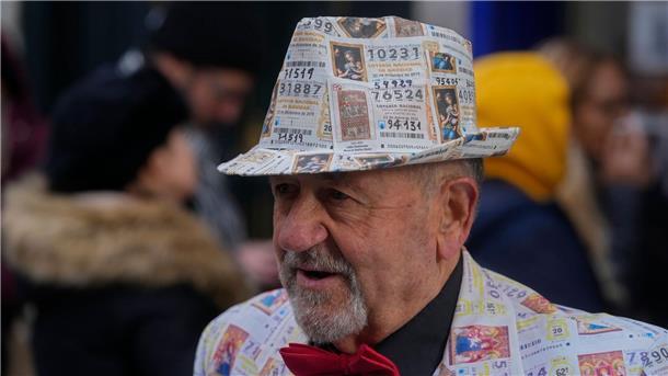 „El Gordo“: Emotionen bei der spanischen Weihnachtslotterie Ein Mann mit einem Anzug und Hut, der mit gedruckten Lottoscheinen verziert ist, steht vor dem berühmten Lotterieladen „Dona Manolita“ in der Innenstadt von Madrid.