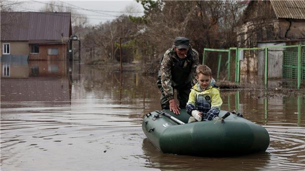 Wasser in russischem Flutgebiet steigt weiter stark an Ein Mann schiebt ein Schlauchboot mit einem Jungen in einem überfluteten Gebiet in Orenburg, Russland.
