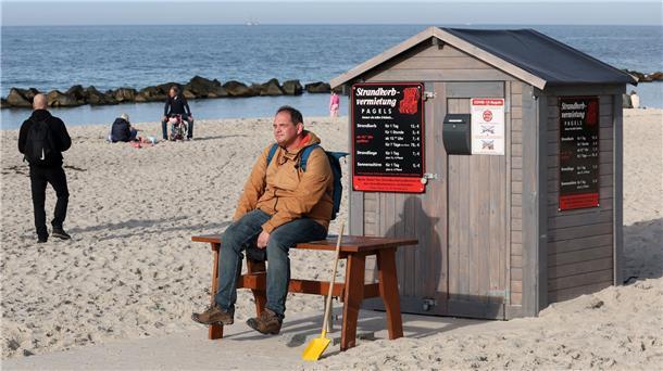 Sommer im Herbst - Oktober endet mit milden Sonnentagen Ein Mann sitzt am Ostseestrand vor dem Häuschen eines Strandkorbvermieters und genießt das warme und sonnige Wetter.