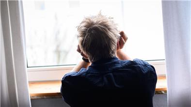 Ein Mann sitzt mit dem Kopf in die Hände gestützt an einem Fenster.