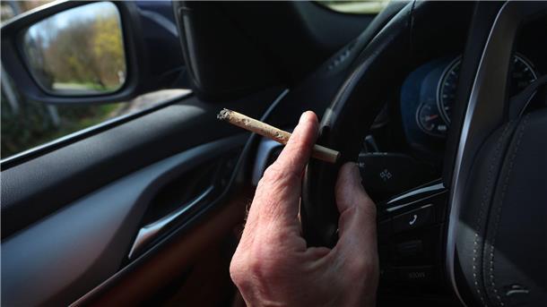 Innenministerin gegen höheren Cannabis-Grenzwert im Verkehr Ein Mann sitzt mit einem Joint zwischen den Fingern am Steuer eines Autos.
