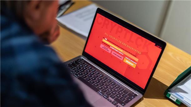 Ein Mann sitzt vor einem Laptop, der mit einem Verschlüsselungstrojaner (Ransomware) befallen ist.